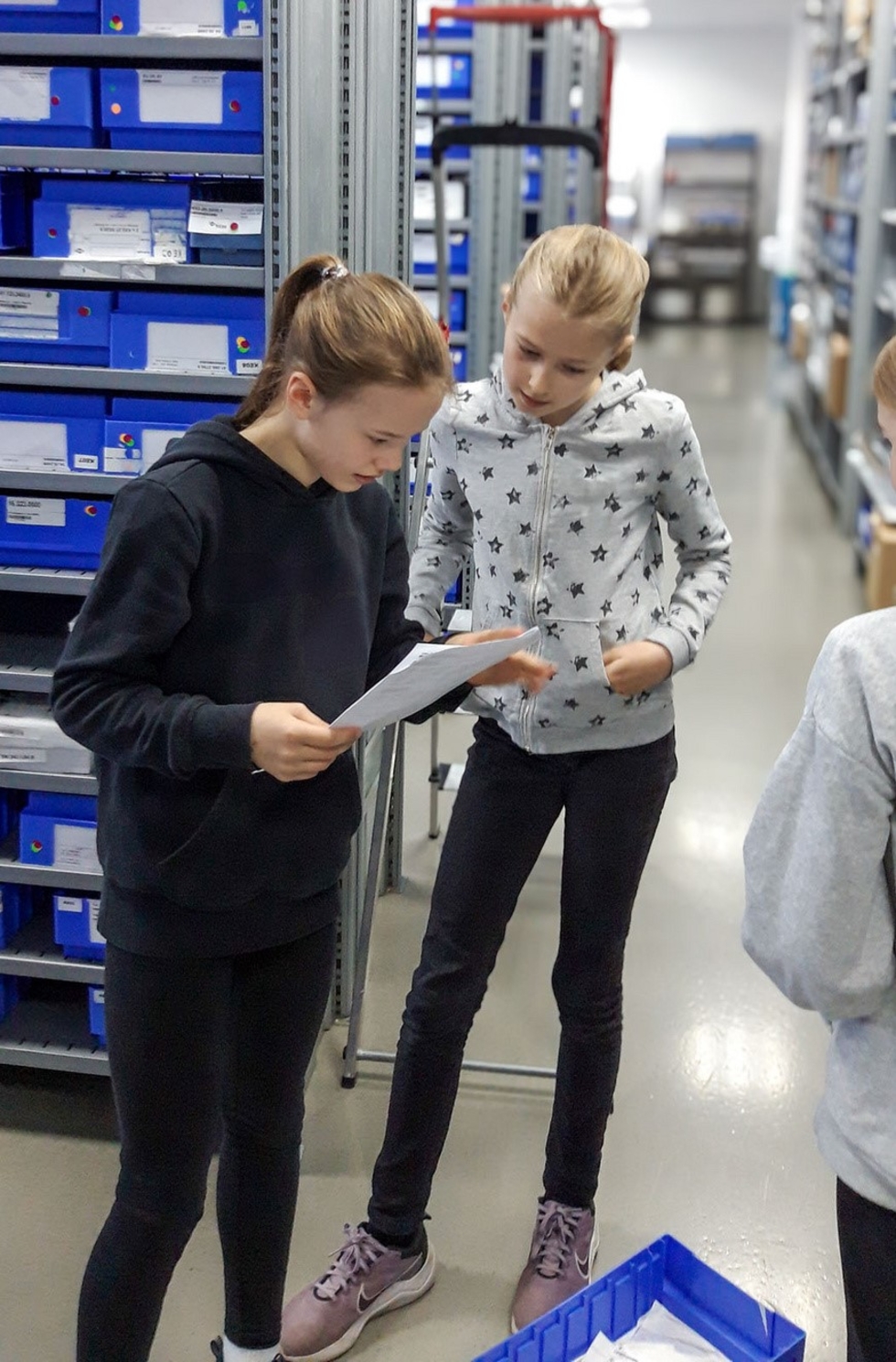 Zwei Girls' Day-Teilnehmerinnen, eines liest einen Auftrag, das andere schaut interessiert zu, in einem technischen Umfeld