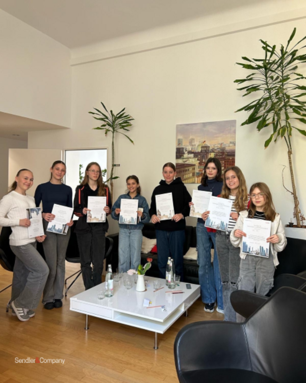 Acht Girls' Day-Teilnehmerinnen stehen in einem modernen Raum und halten Zertifikate, im Hintergrund Pflanzen und ein Bild an der Wand.