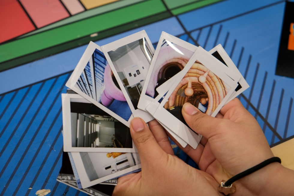 Hände halten eine Sammlung von Polaroid-Fotos, die verschiedene Innenräume und architektonische Details zeigen.