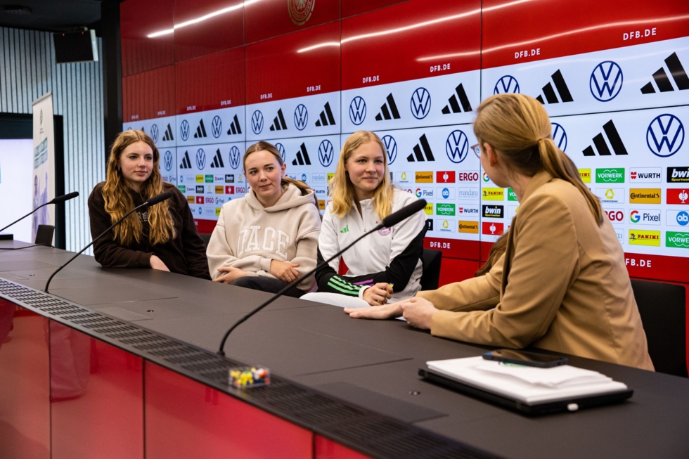 Vier Frauen sitzen an einem Tisch vor einer Wand mit Logos.