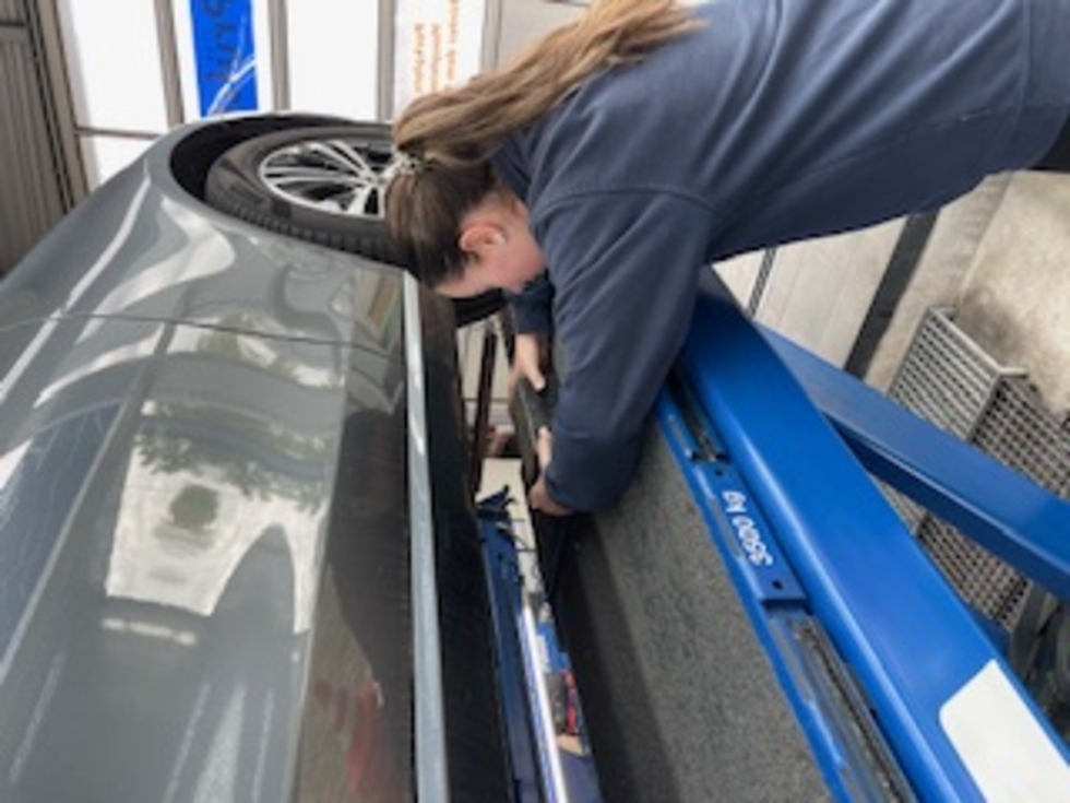 Girls'Day-Teilnehmerin prüft eine Auto auf der Hebebühne