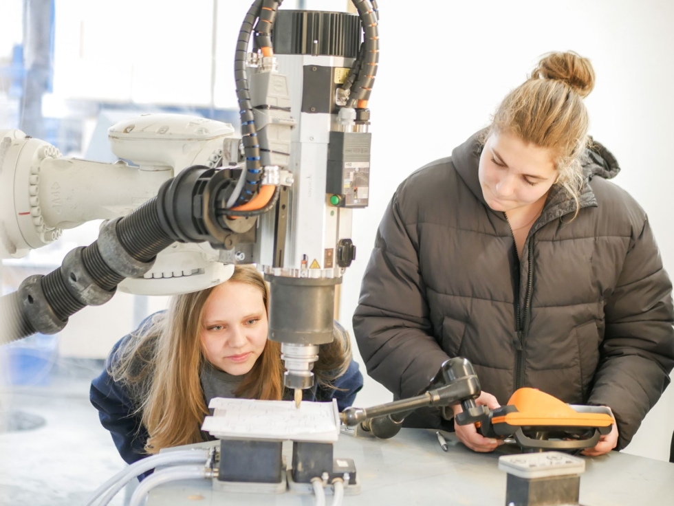 Zwei junge Frauen arbeiten in einer Werkstatt an einer Maschine.
