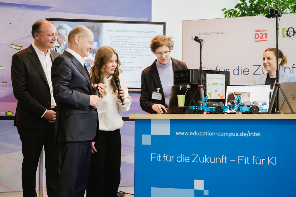Mehrere Personen stehen zusammen mit Bundeskanzler Scholz um einen Getränkeautomaten herum