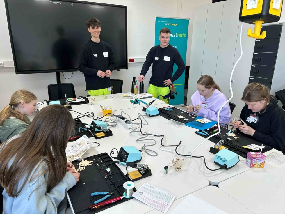 Girls' Day Teilnehmerinnen sitzen an einem Tisch und fertigen ein elektronisches Gespenst an unter Anleitung der Mitarbeiter
