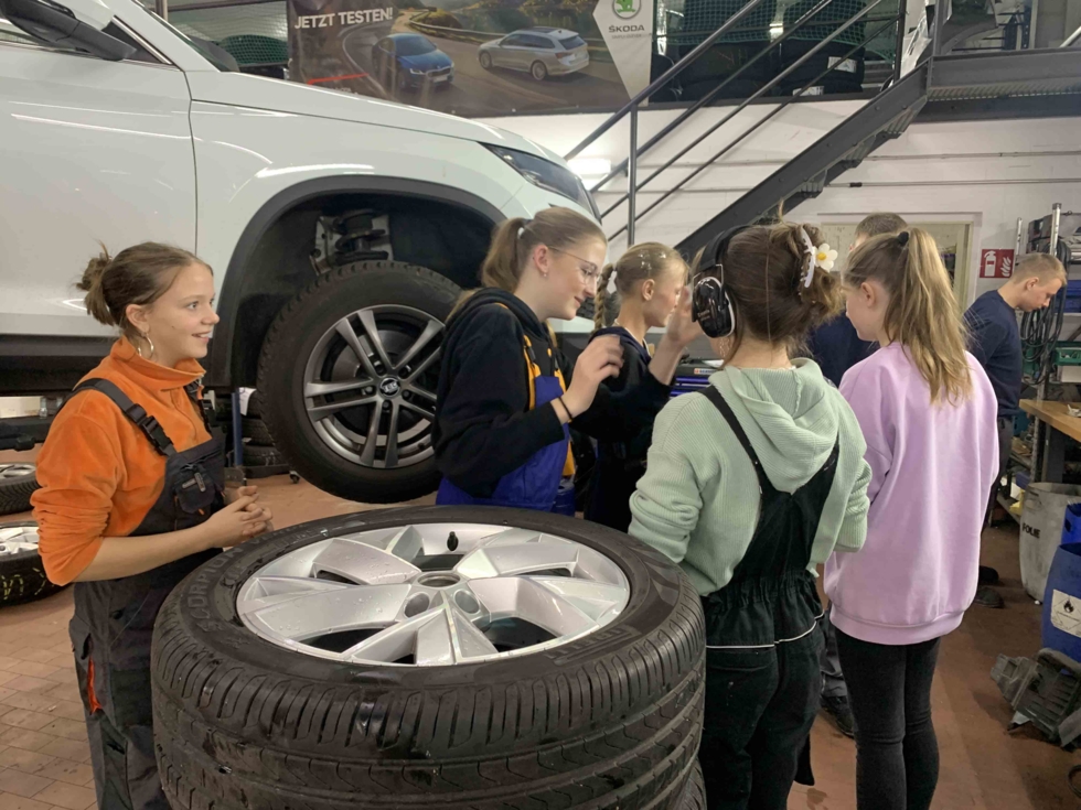 Girls'Day-Teilnehmerinnen in einer Kfz-Werkstatt vor Autoreifen