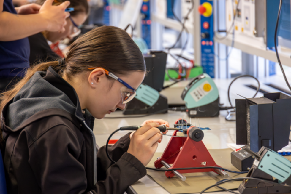 Girls' Day-Teilnehmerin arbeitet konzentriert an einem Leuchtschild mit Lötkolben in einer Ausbildungswerkstatt für Metall, Elektro und IT