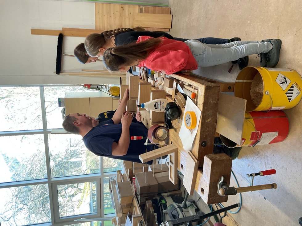 Girls' Day-Teilnehmerinnen beobachten einen Schreiner bei der Arbeit in einer Werkstatt.