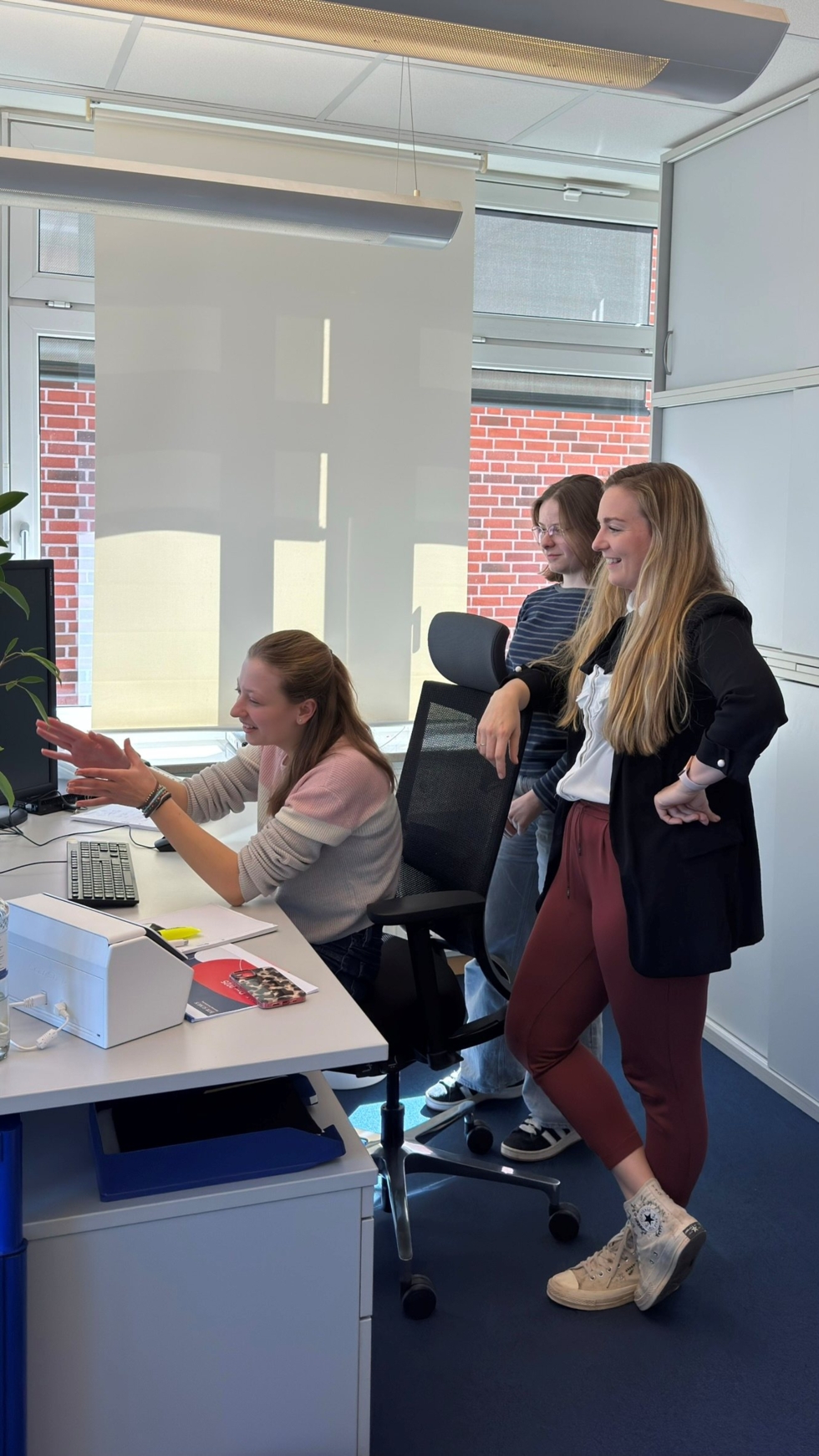 Drei Teilnehmerinnen des Girls' Day arbeiten am Computer in einem modernen Büro. Eine sitzt am PC, während die anderen stehen und zuschauen.
