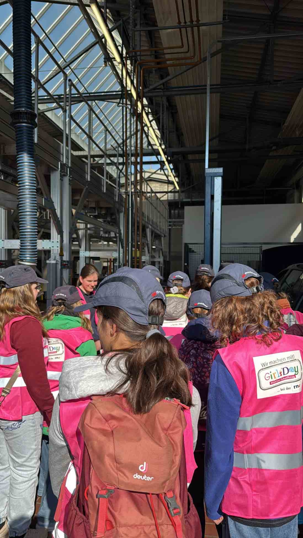 Girls'Day-Teilnehmerinnen mit Warnwesten von hinten fotografiert in einer Werkhalle