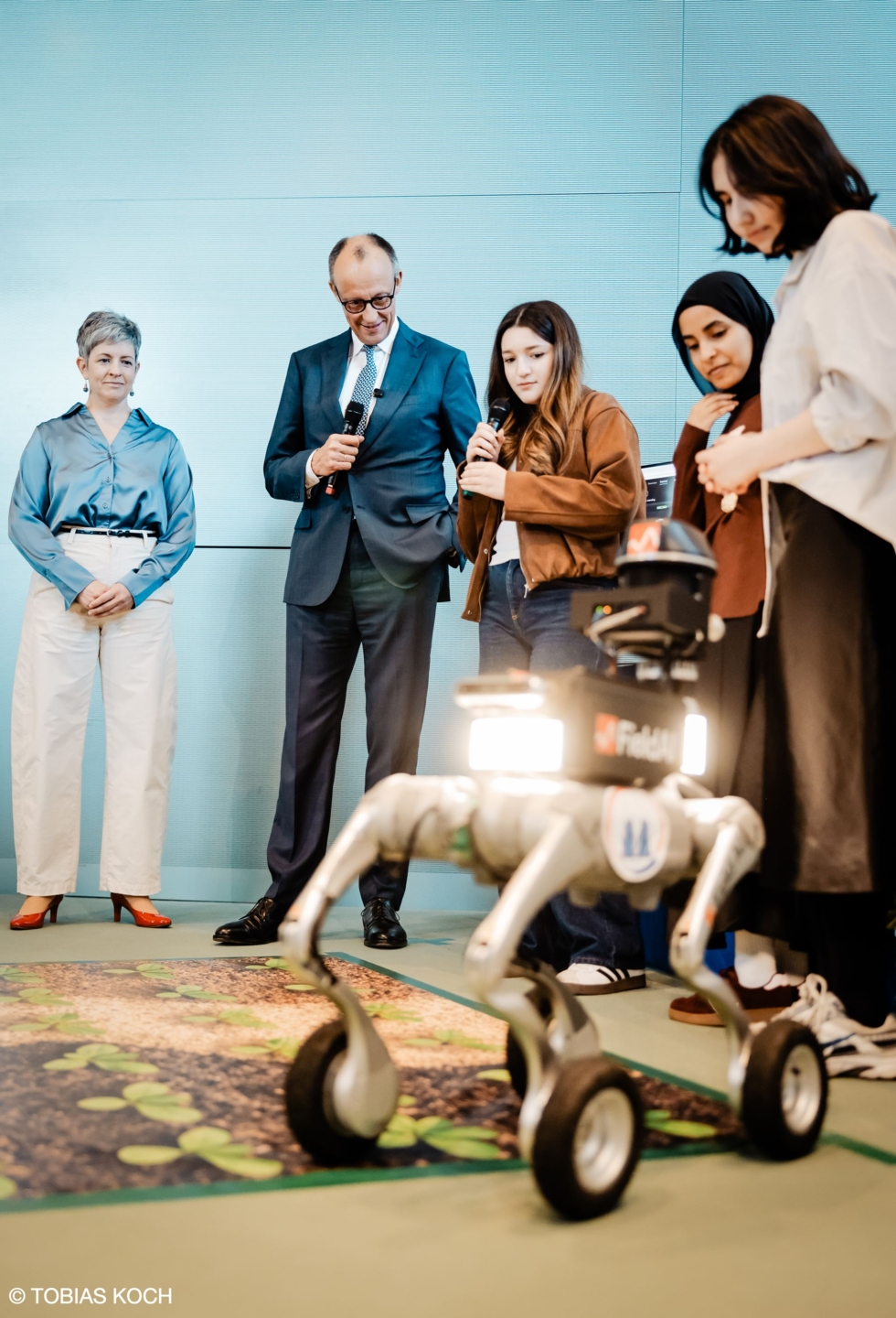 Bundeskanzler Merz, Girls'Day-Teilnehmerinnen mit Roboter im Vordergrund