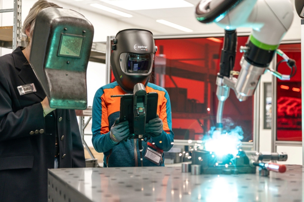 Girls' Day-Teilnehmerinnen im modernen Maschinenbau, eine trägt einen Schweißhelm und hält ein Gerät, während eine andere Person daneben steht