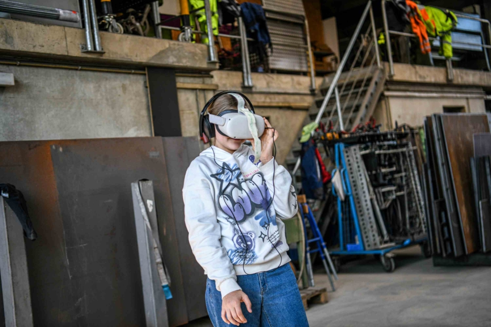 Junge Person mit VR-Headset in einer Werkstatt, umgeben von Werkzeugen und Maschinen.