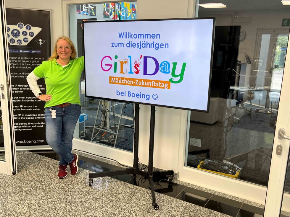 Mitarbeiterin neben Girls'Day-Screen mit Wilkommensgruß