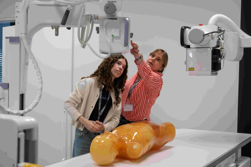Girls' Day-Teilnehmerin steht an einem Tisch mit einem anatomischen Modell, während die Mitarbeiterin eine medizinische Maschine erklärt. Die Szene zeigt eine interaktive Gesundheitsveranstaltung.