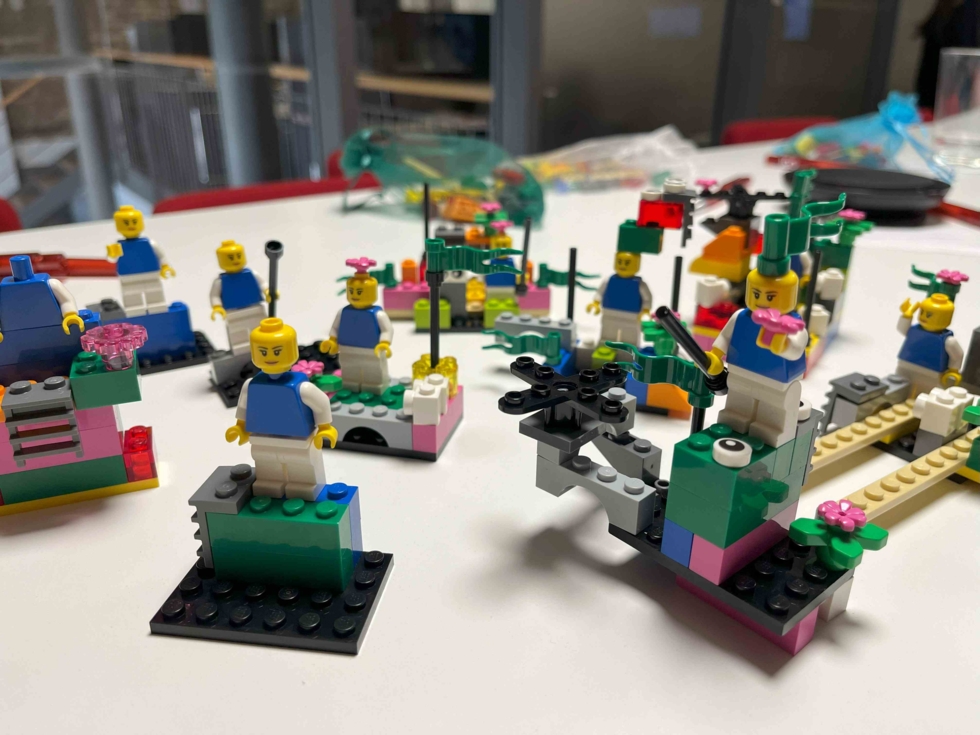 Bunte LEGO-Szenen mit Figuren, Blumen und verschiedenen Strukturen auf einem Tisch.
