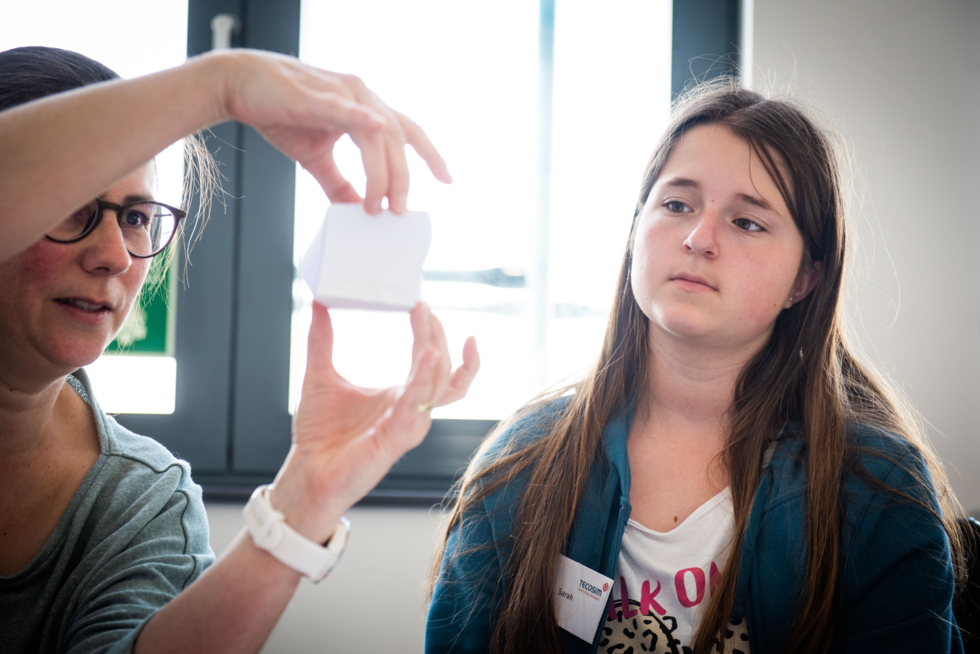 Eine Person hält einen Würfel aus Papier in der Hand, eine andere schaut sich diesen an.