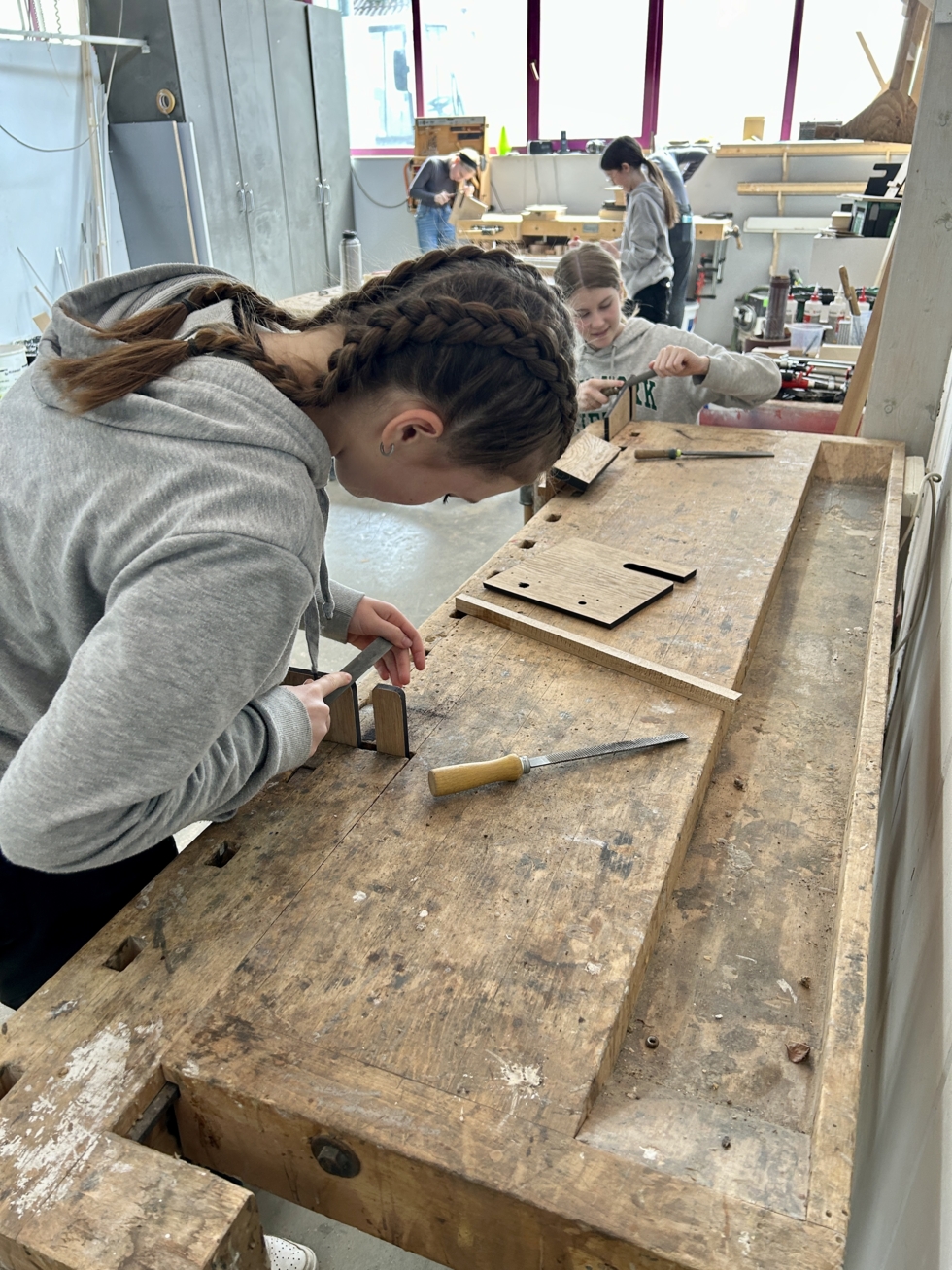 Mädchen an einer Werkbank feilen Holzteile.