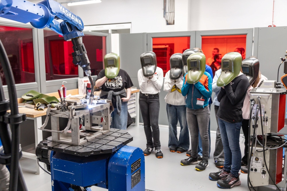 Girls' Day-Teilnehmerinnen mit Schweißhelmen beobachten einen Roboter im modernen Maschinenbau