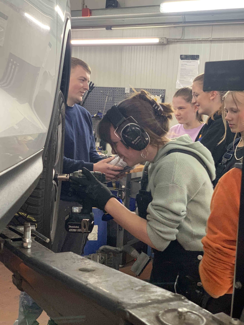Girls'Day-Teilnehmerin und Mechaniker schrauben an einem Auto