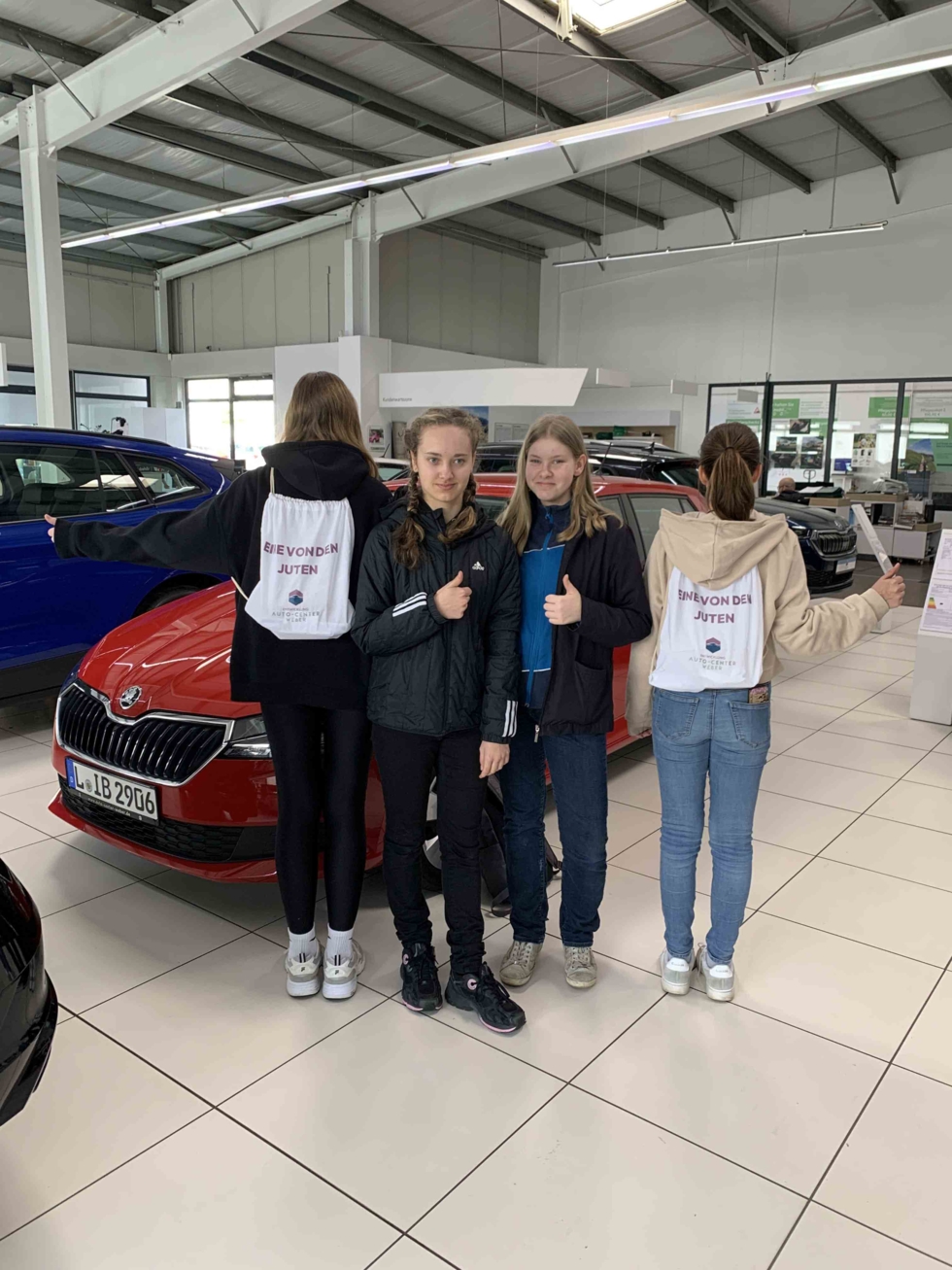 Girls'Day-Teilnehmerinnen mit Dauemn hoch und Autocentertaschne im Verkaufsraum