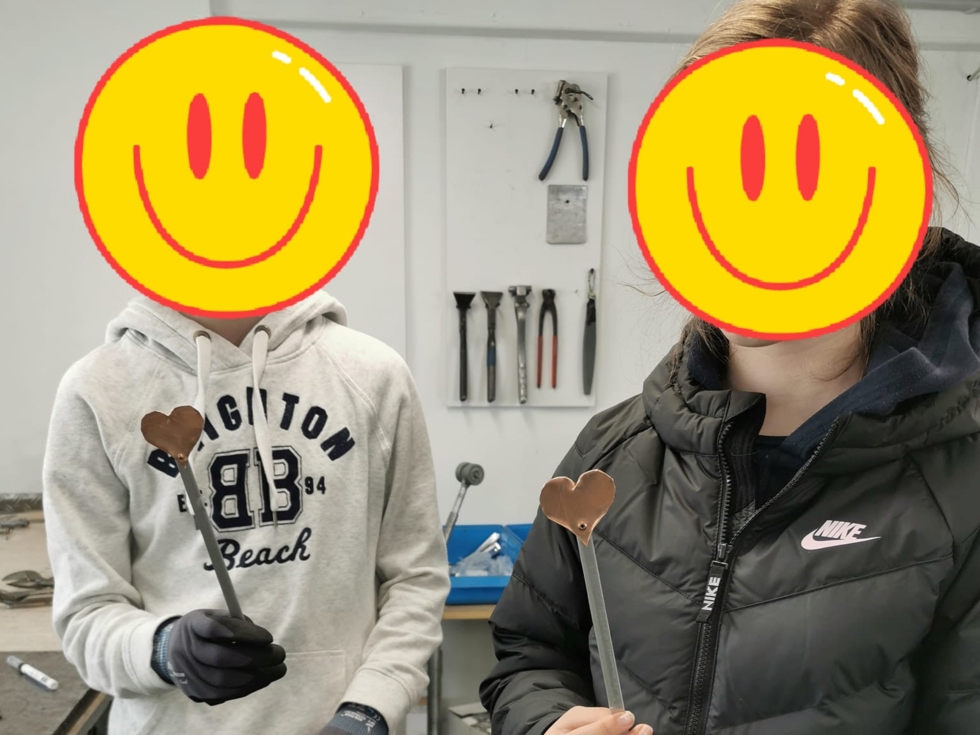 Zwei Personen mit Smiley-Köpfen halten jeweils ein Blechherz mit Stab in der Hand