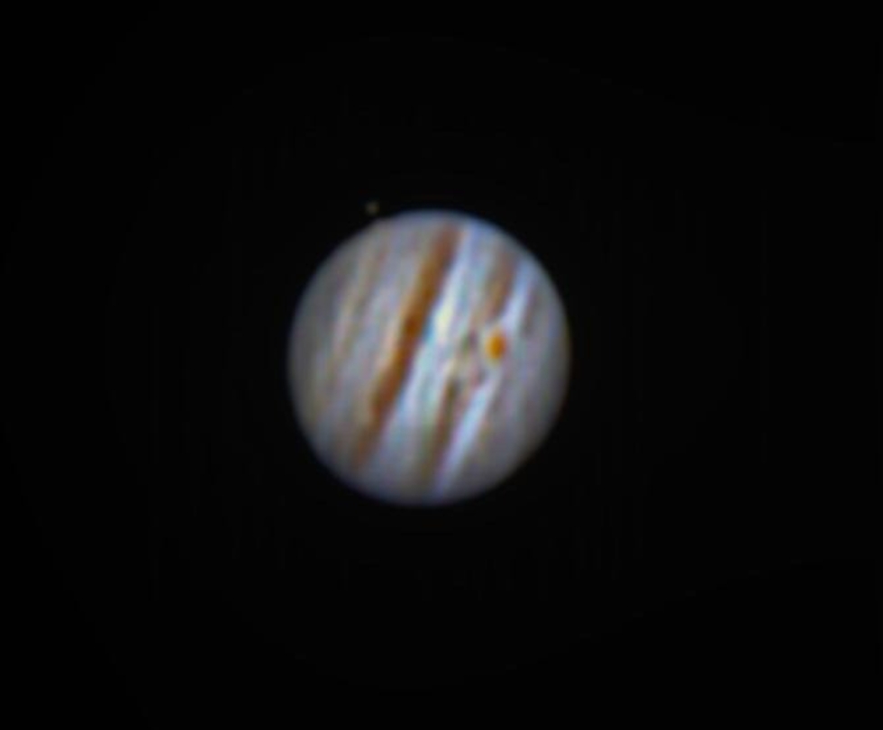 Nahaufnahme von Jupiter mit sichtbaren Wolkenbändern und einem seiner Monde im Hintergrund, aufgenommen durch ein Teleskop