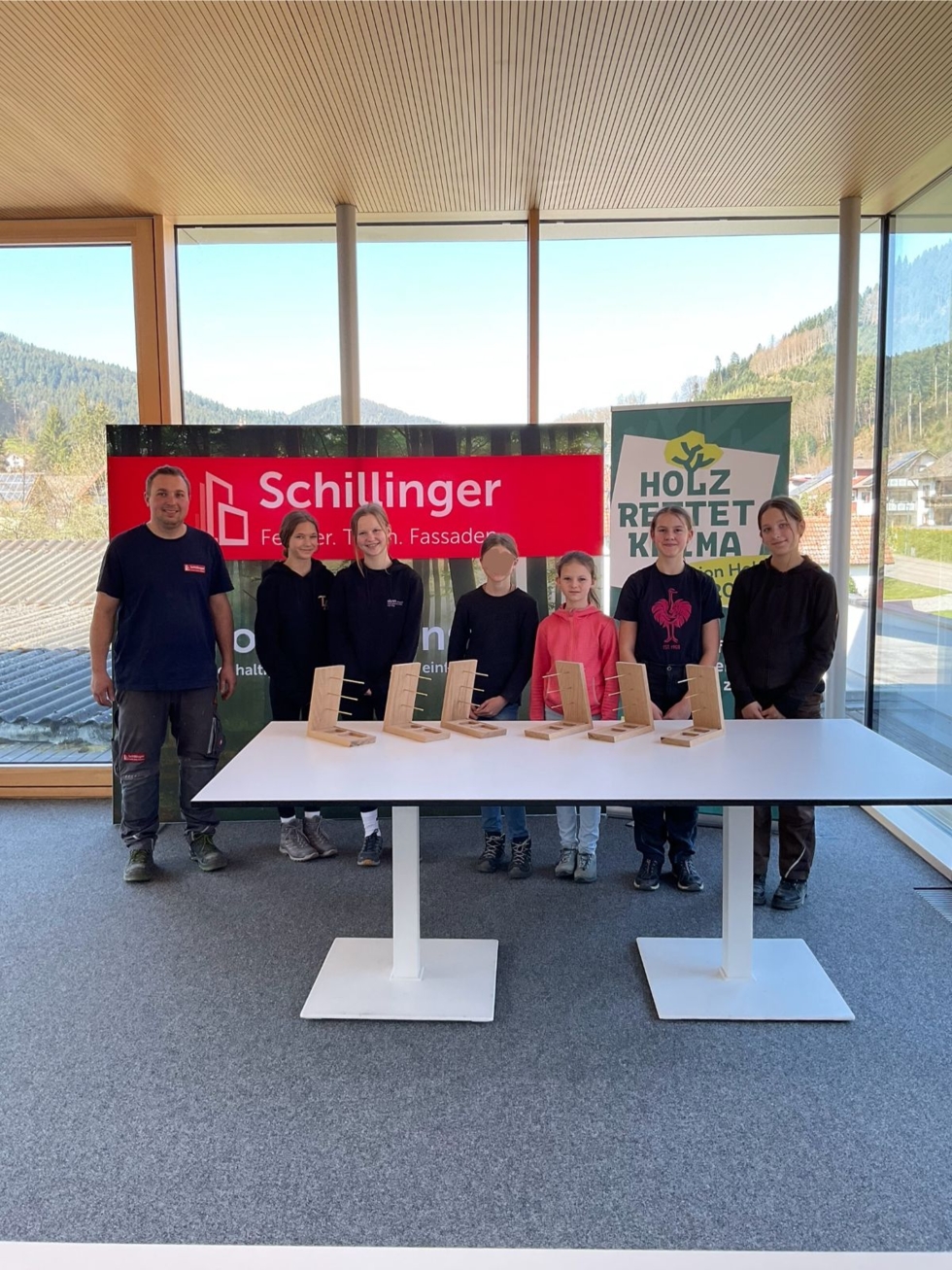 Teilnehmerinnen des Girls' Day präsentieren zusammen mit Mitarbeitenden selbstgebaute Schmuckständer an einem Tisch