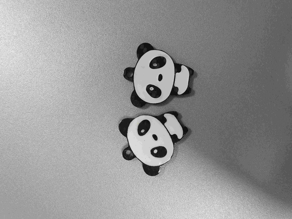 Zwei Schlüsselanhänger in Form von Pandas, aus Carbon gefertigt, auf einer grauen Oberfläche