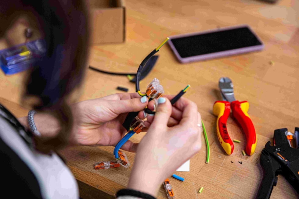 Eine Girls' Day-Teilnehmerin bastelt in einer Elektrowerkstatt mit elektrischen Bauteilen. Werkzeuge wie Zangen und Kabel sind sichtbar
