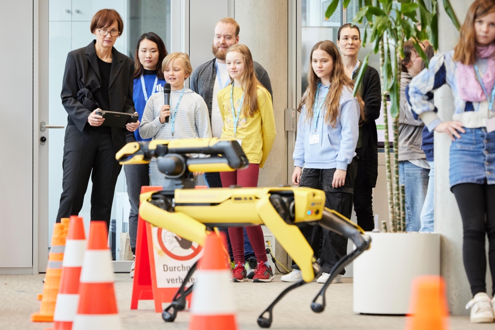 Im Vordergrund ein Roboter-Hunde, dahinter eine Gruppe von Mädchen mit der Ministerin